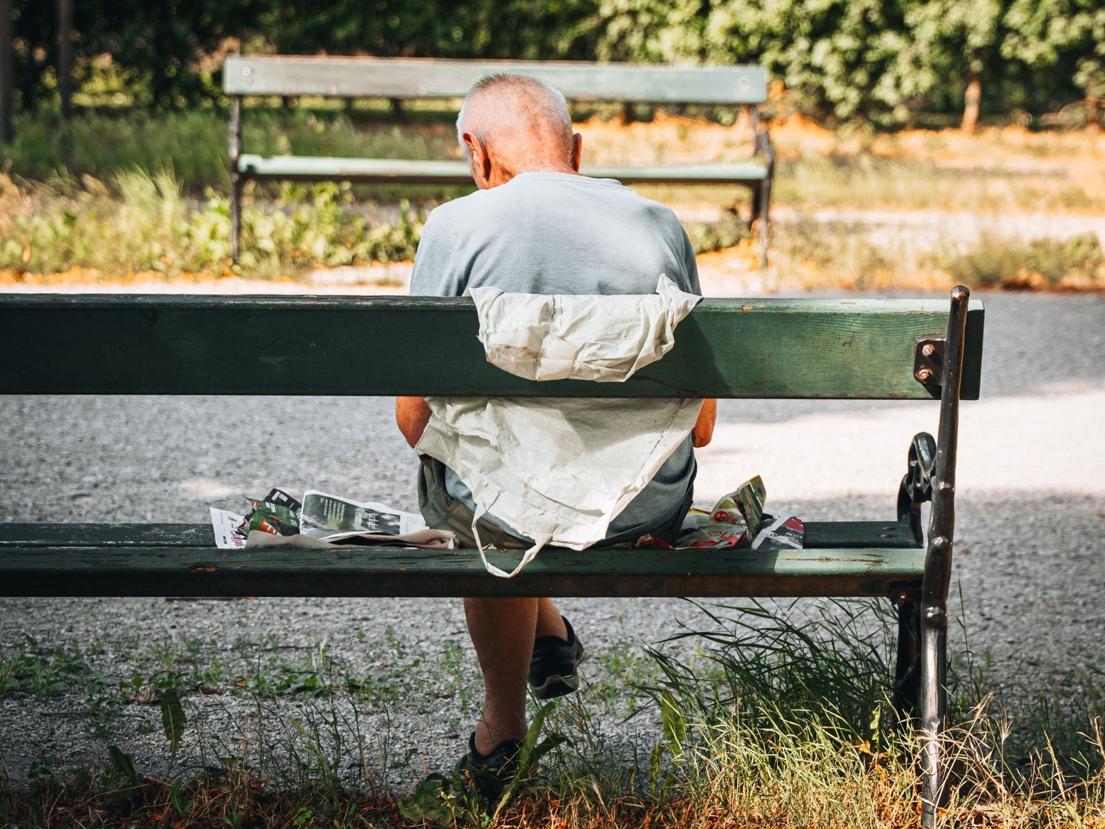 Älterer Mann sitzt auf einem grünen Bankerl in einem Wiener Park