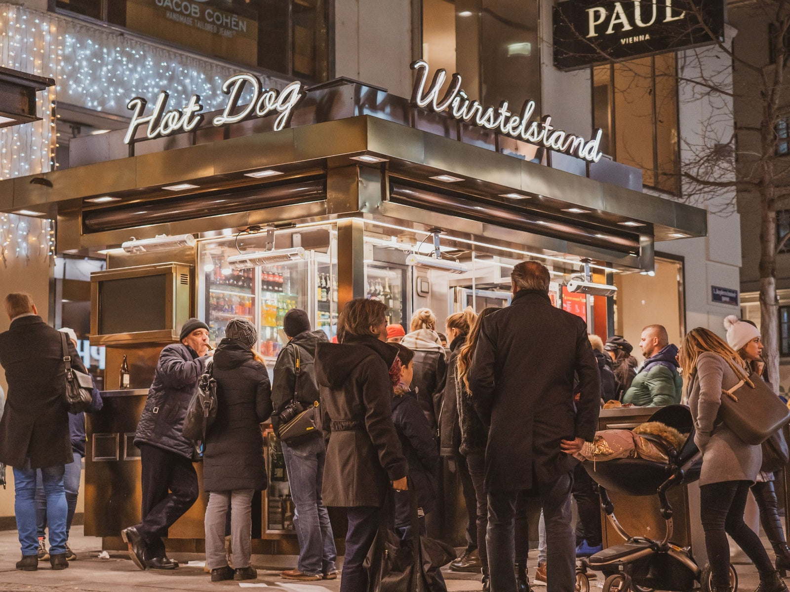 Menschen stehen nachts an einem Wiener Würstelstand und bestellen Essen