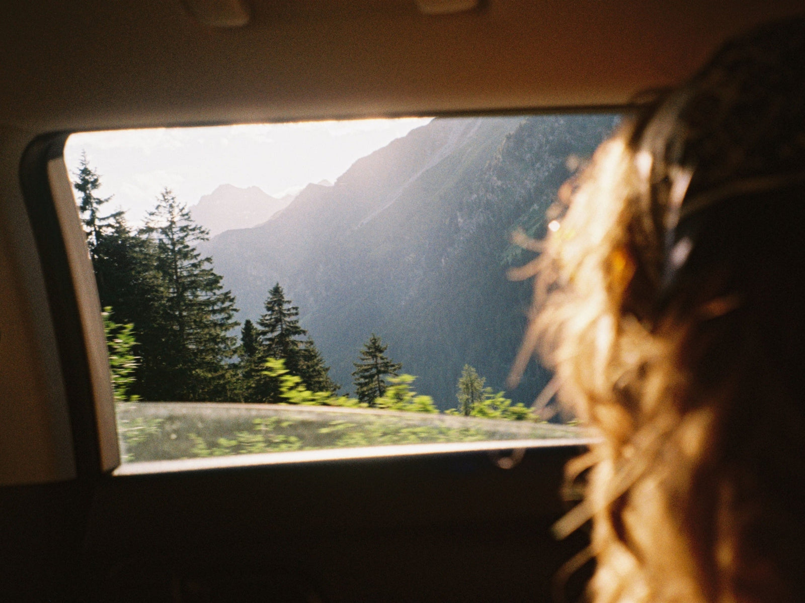 Blick aus dem Autofenster auf eine sonnige Berglandschaft während einer Reise
